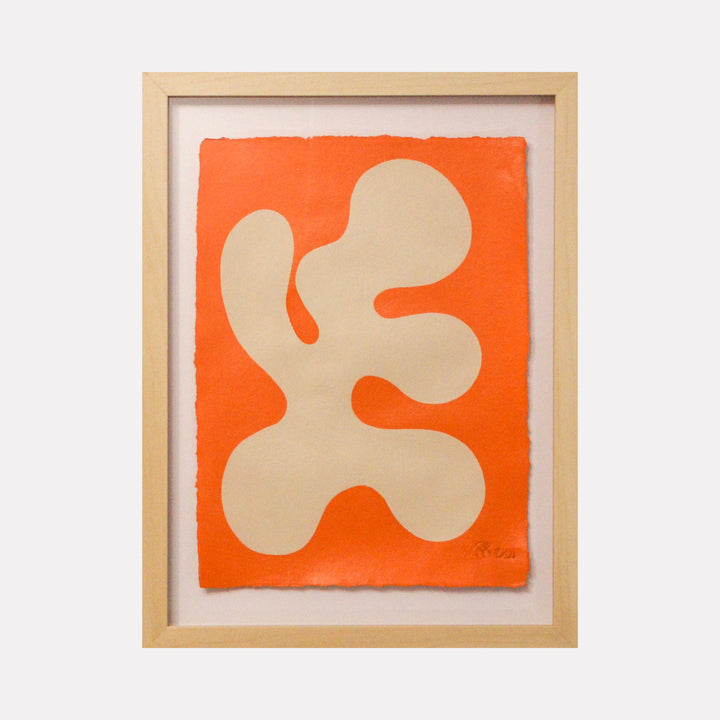 The artwork 'Stillness I' by Shadia Sabagh features an organic abstract beige form against a vibrant orange background, painted in acrylic on handmade cotton paper. The minimalist composition showcases a flowing, amoeba-like shape with curved edges, framed in natural wood, creating a striking contrast between warm tones. By Shadia Sabagh.