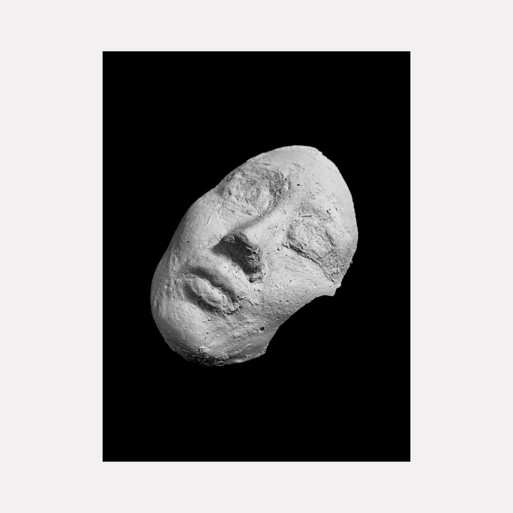 The artwork 'That Time We Met' by Garrett Carroll features a dramatic black and white photograph of a sculptural plaster mask fragment against a deep black background. The textured, rough surface of the white plaster creates a striking contrast, capturing subtle shadows and highlights that reveal the mask's dimensional features, photographed at an angle that suggests movement and ethereal presence.