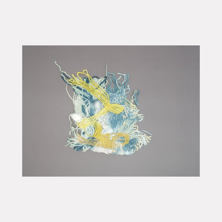 The artwork 'Untitled 172' by Victoria Manganiello features an abstract composition of intertwining fibers in yellow and light blue hues. The textile piece displays flowing, organic patterns with wispy strands creating dynamic movement against a gray background. Natural and synthetic fibers are woven together in a 9x9 inch format, showcasing a delicate interplay of textures and dyes.