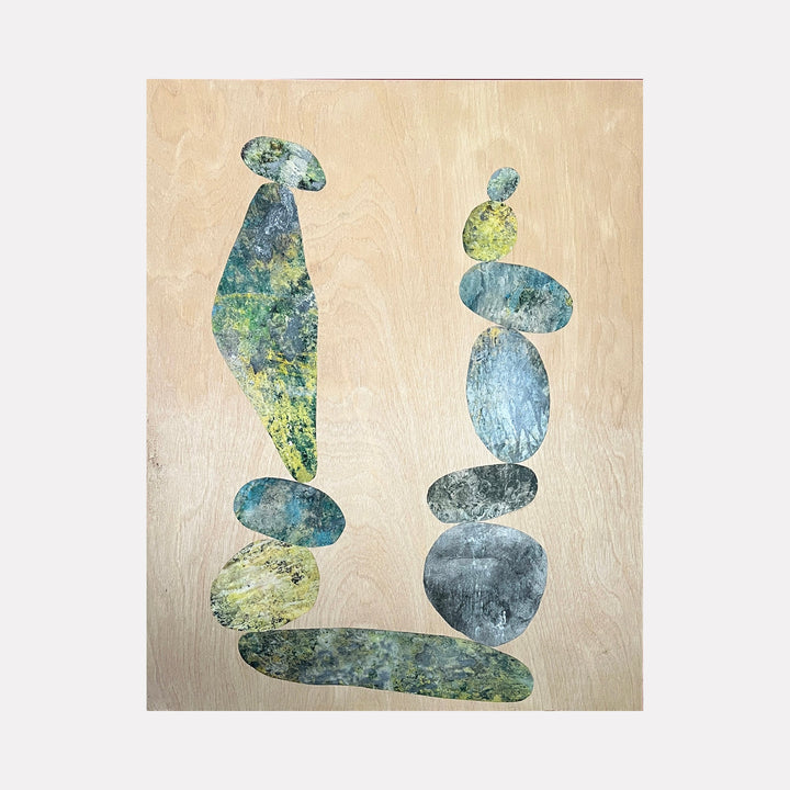 The artwork 'Cairn For John' by Sunny Chapman features abstract balanced stone formations in mottled blue-green and gray tones against a warm beige background. Two vertical stacks of organically shaped rocks create a harmonious composition, combining collaged alchemic prints with acrylic on wood panel to achieve a textured, meditative quality.