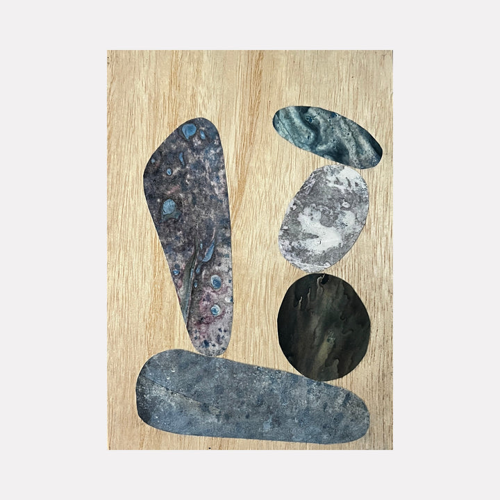 Carled Cairn by Sunny Chapman features abstract stone-like shapes in muted blues and grays arranged on a natural wood panel. The composition includes organic forms resembling stacked cairn stones, with textured surfaces suggesting weathered minerals, created using acrylic and alchemic print collage techniques on wood.