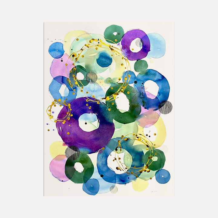 The artwork 'In Harmony' by Jocelyn Benford features vibrant watercolor circles in blues, purples, and greens, interconnected by flowing golden lines. Abstract floating rings create a dynamic composition with translucent layering effects. White negative spaces and delicate black speckles add depth to this mixed media piece on paper.