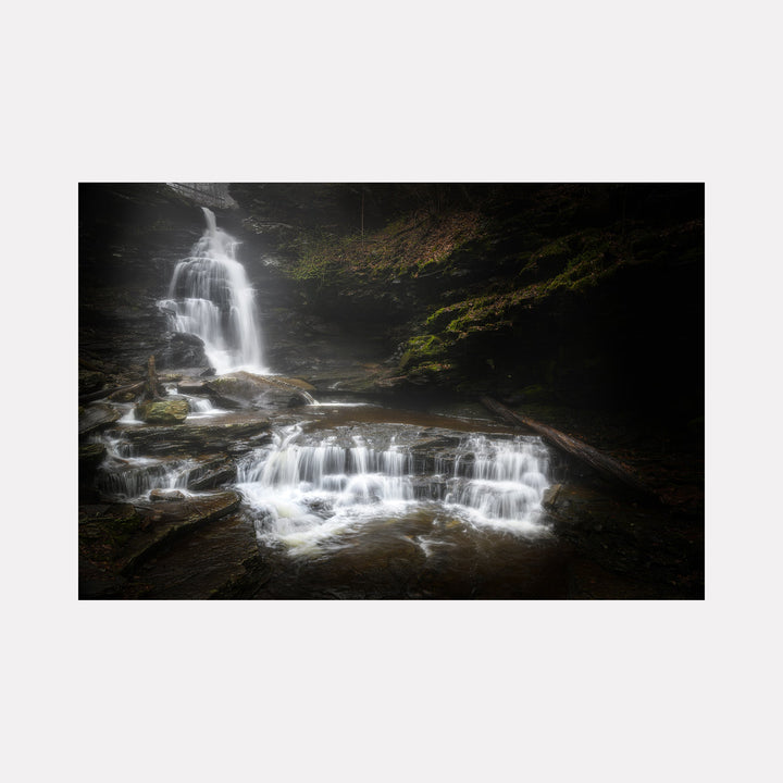 The artwork 'Steps of Eternity' by Dennis Maida captures a dramatic cascading waterfall photographed in moody lighting. Multiple tiers of white water flow over dark rocky ledges, creating a stepped effect. Misty water tumbles down moss-covered stone formations, surrounded by shadowy forest vegetation, producing a mesmerizing natural composition.