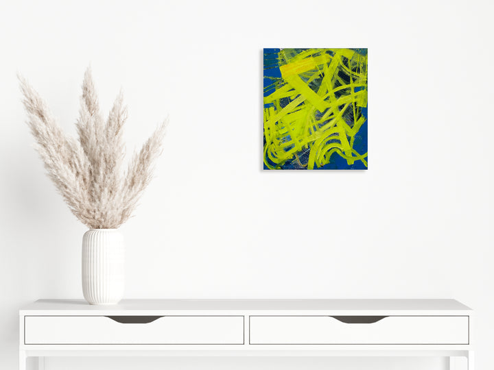 The artwork 'Compassed' by Julie Shapiro features dynamic neon yellow brushstrokes swirling against a deep cobalt blue background. The abstract oil painting showcases energetic gestural marks creating a sense of movement and direction, with bold contrasting colors merging in an expressive contemporary style on canvas.