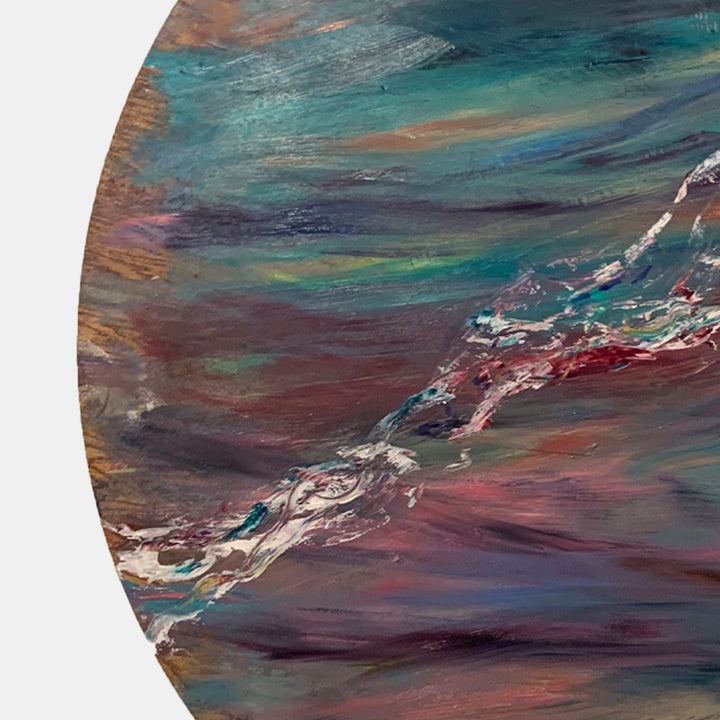 The artwork 'Impressions of Light 2' by Jadie Meprivert features a dynamic circular composition with swirling brushstrokes in turquoise, burgundy, and copper tones. Abstract waves of color create a fluid movement across the wooden surface, with a striking diagonal white streak cutting through deep maroon layers, showcasing textural oil paint application at 48x48 inches.