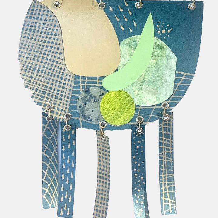 The artwork 'Juxtaposition' by Sunny Chapman features abstract geometric shapes in teal, cream, and lime green, with textured grid patterns and metallic accents. Silver grommets connect hanging paper strips decorated with raindrop patterns and dotted textures, creating a dynamic mixed-media composition on metallic paper.